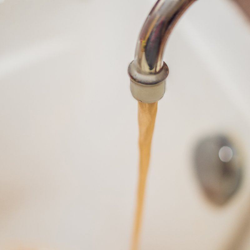 dirty brown water running from a kitchen tap into a sink